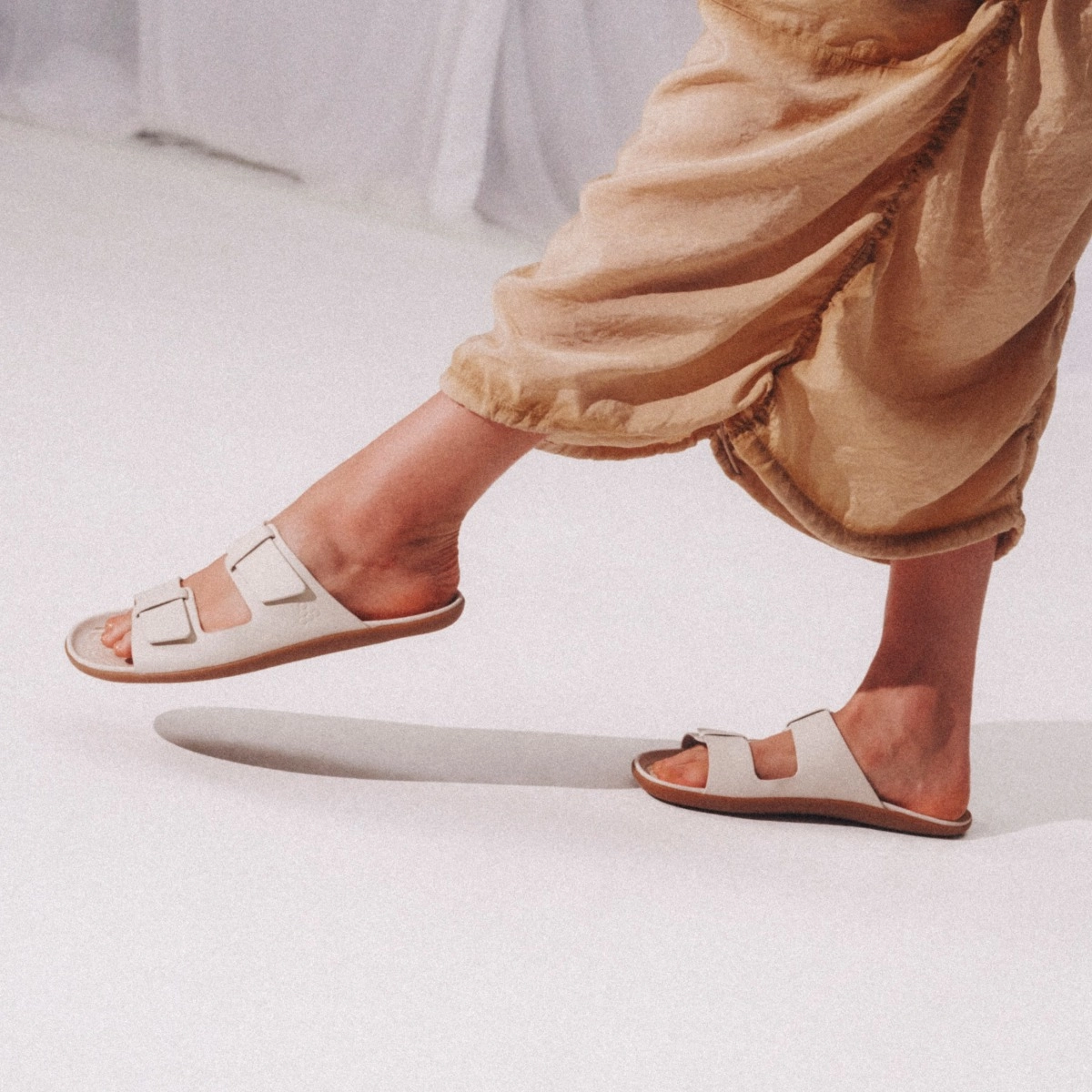 Close-up of the VivoBarefoot Sensus Yin slide sandal in sand worn with linen, from the Spring/Summer 2026 lookbook.